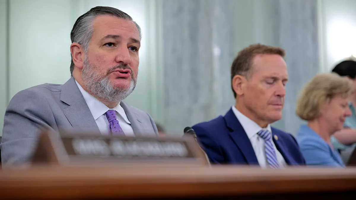 A senator speaks sitting down next to other senators that are slightly blurred.