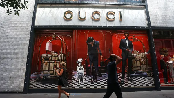 Pedestrians walk past a Gucci retail store window.