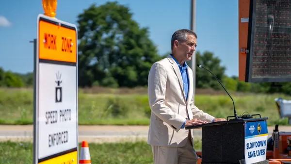 A man speaks at a podium next to road signs.