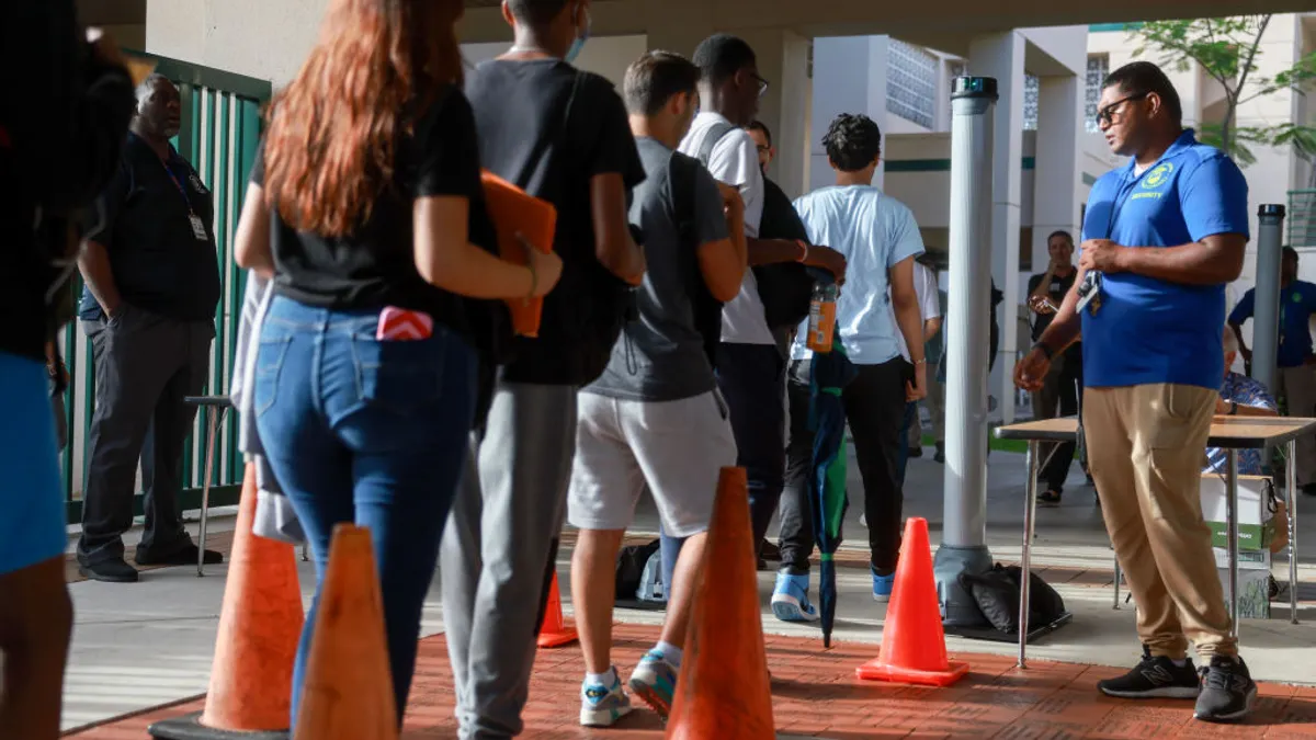 Students are seen from behind as they walk through a weapons detection system outside a school building.