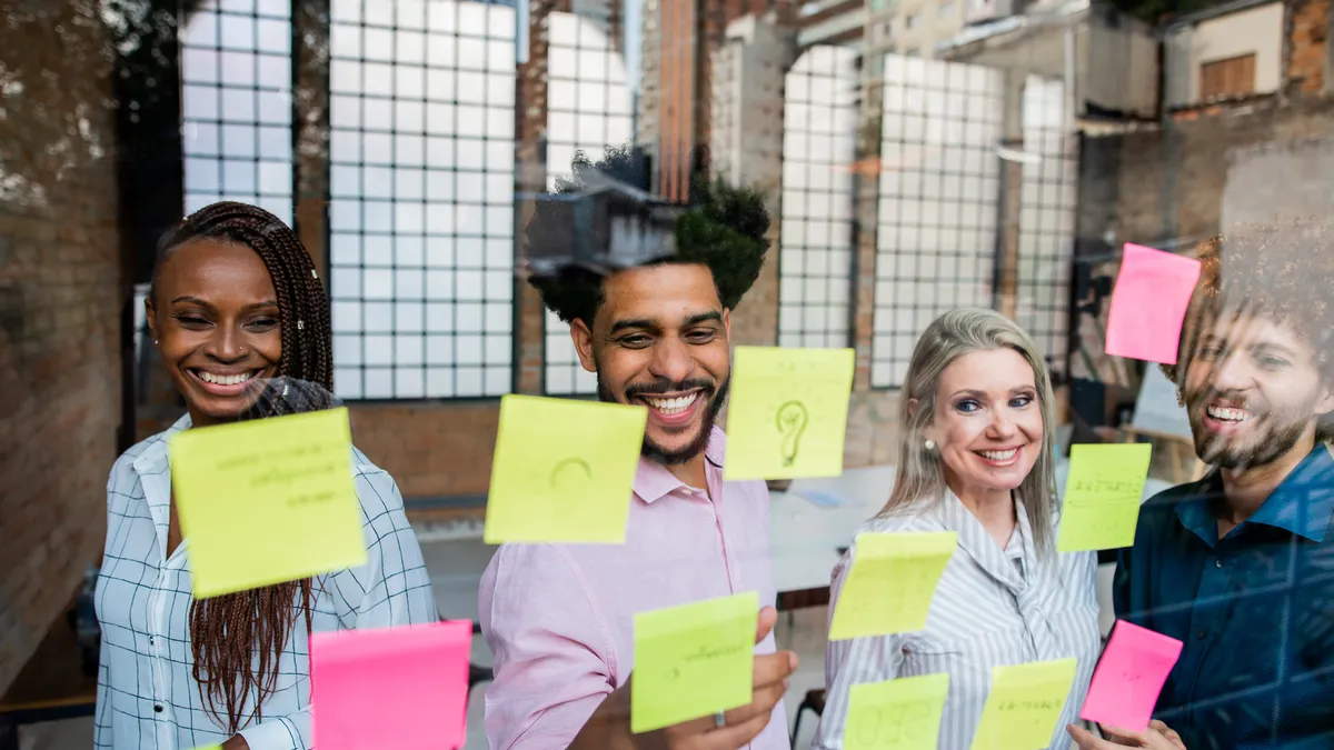 A group of coworkers put post-it notes on a wall as part of a brainstorming session