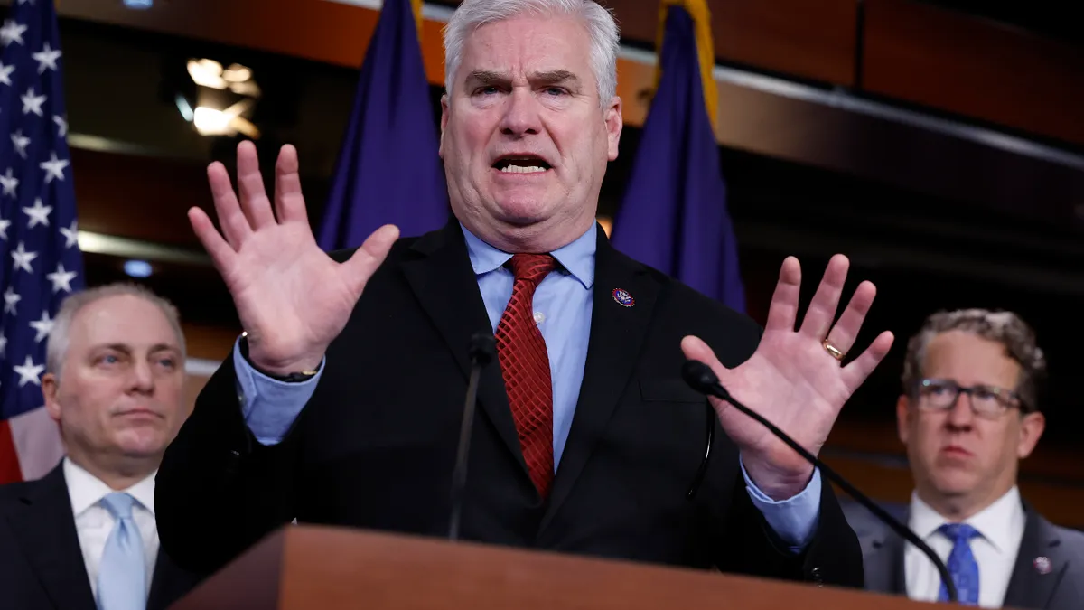 U.S. Rep. Tom Emmer holds up his hands while standing at a podium.