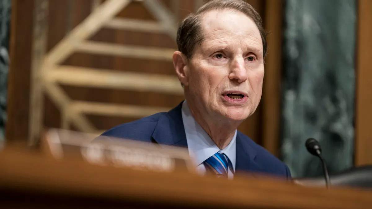 Sen Ron Wyden sits behind a wooden podium with a microphone.