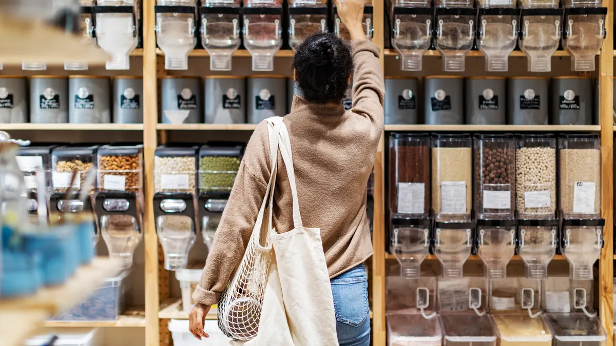 Back of shopper reaching toward a refillable food container in a store.