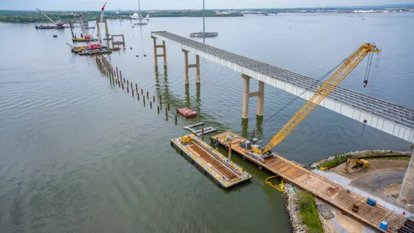 In a gray body of water, tall metal structures on concrete rise out into the air.