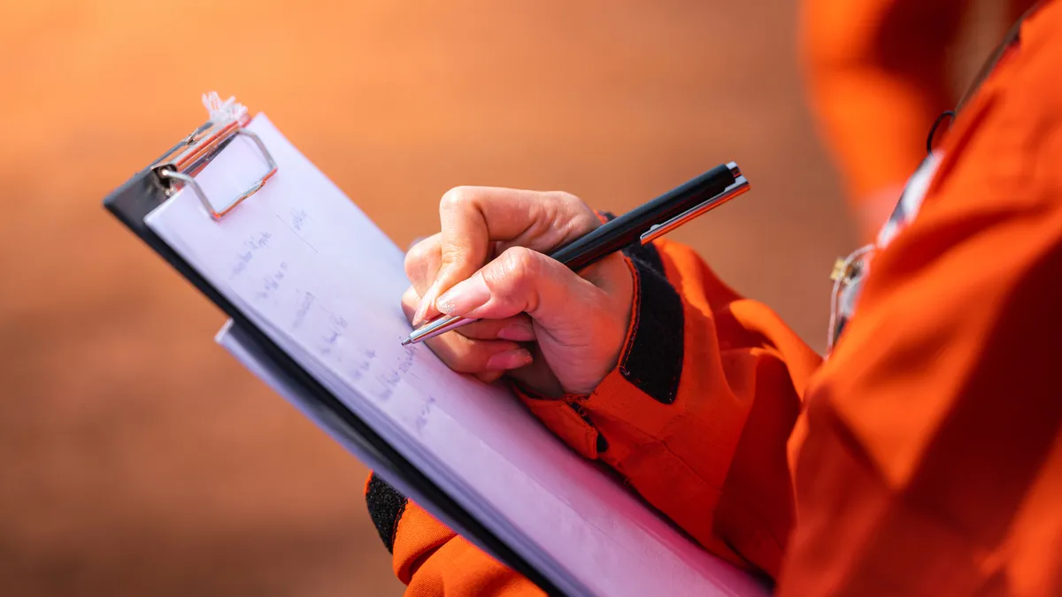 A safety officer writes a note on a checklist paper as part of a worksite audit and inspection.