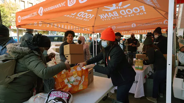 People standing under a tent hand out food in bags and boxes.