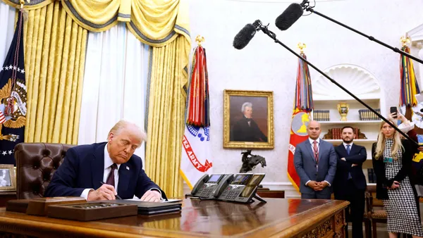 President Trump signs an executive order in the oval office of the white house as staffers and press look on