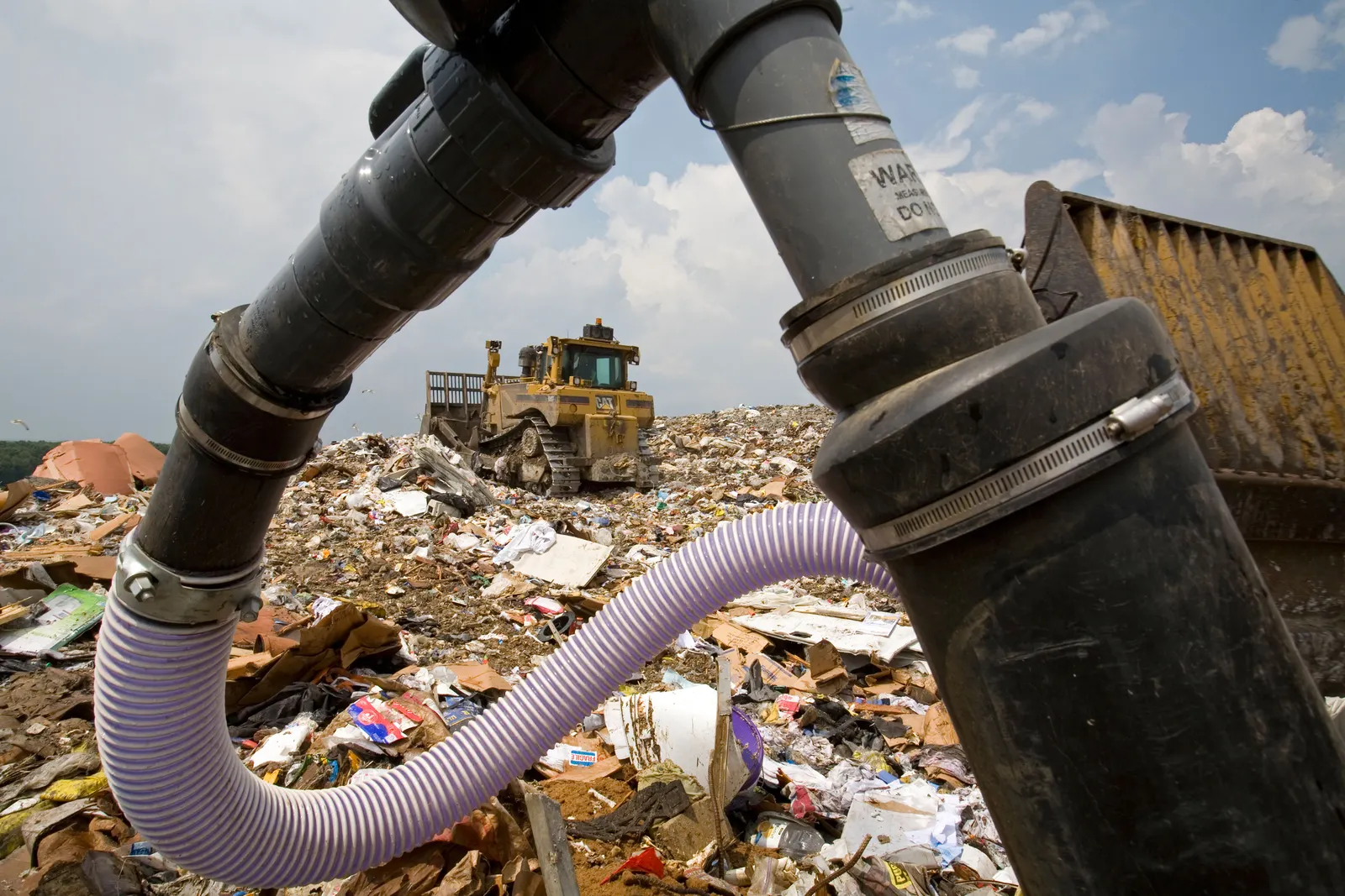 A landfill gas well in foreground, landfill equipment and waste in background