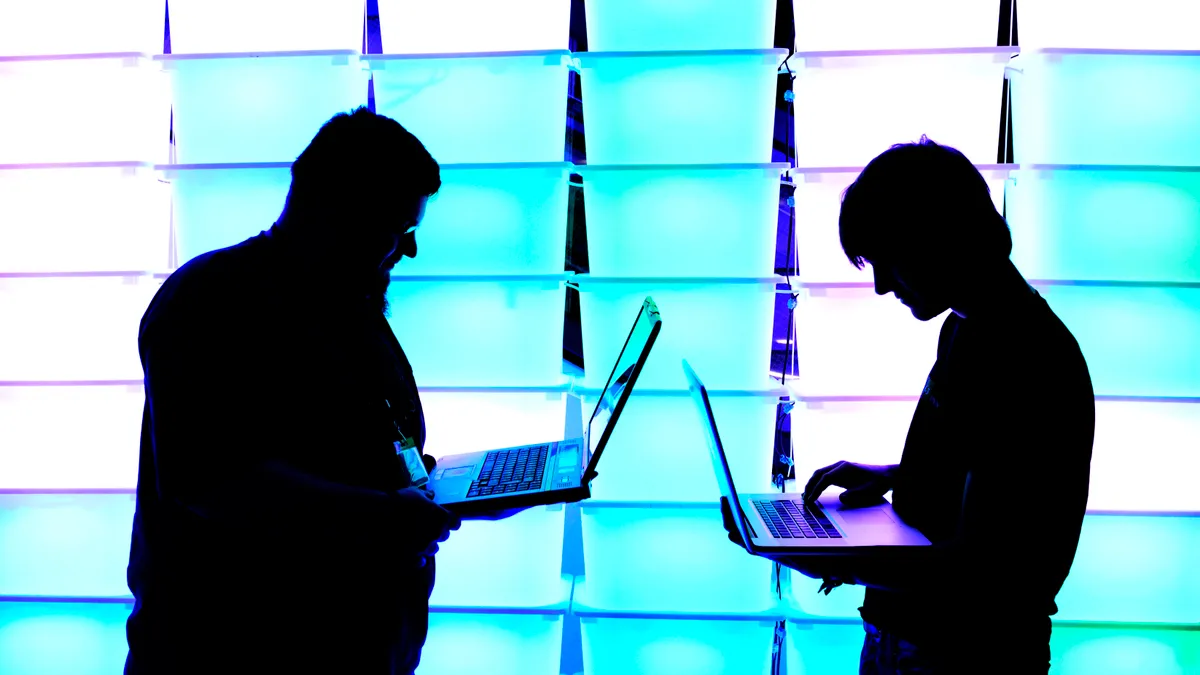 Two figures facing each other with laptops