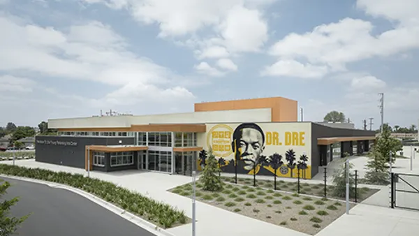 The exterior of a building with greenery and a parking lot. The face of a man appears on the side of one building captioned "Dr. Dre".