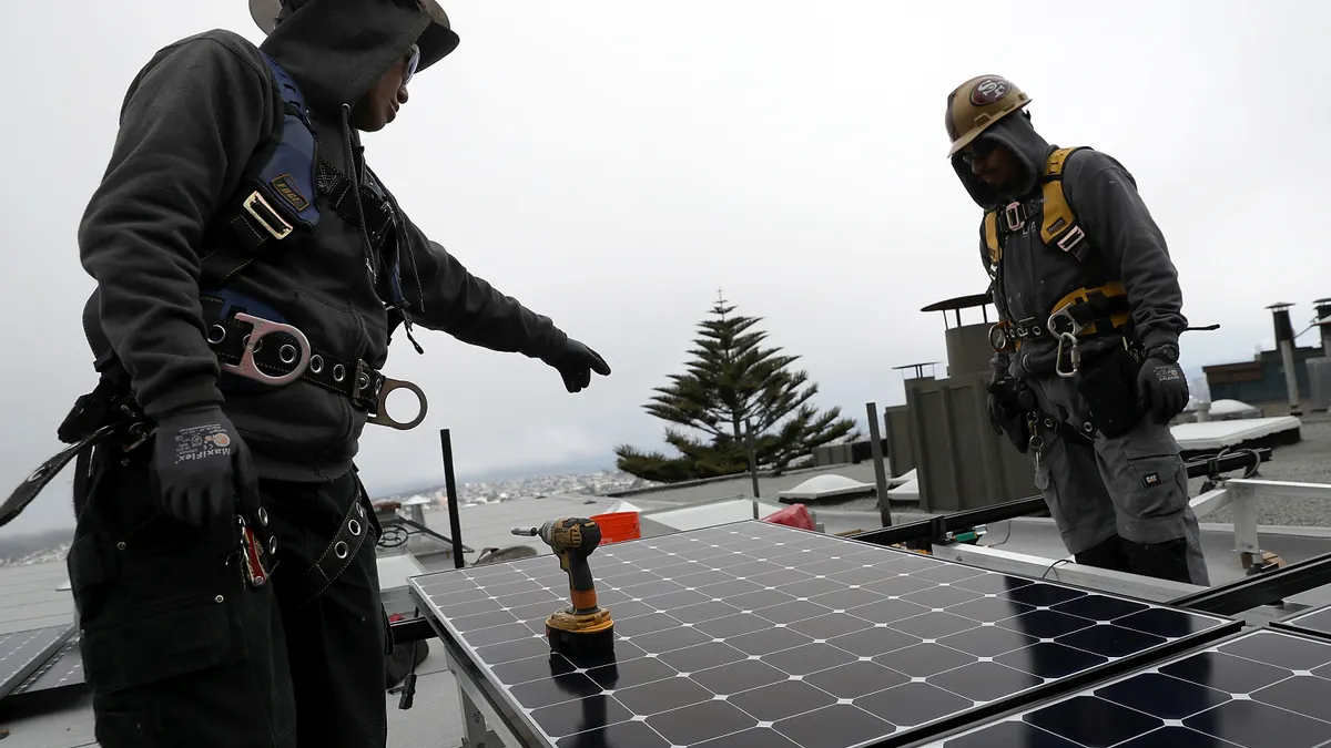 A worker points to a solar panel while another worker looks on.