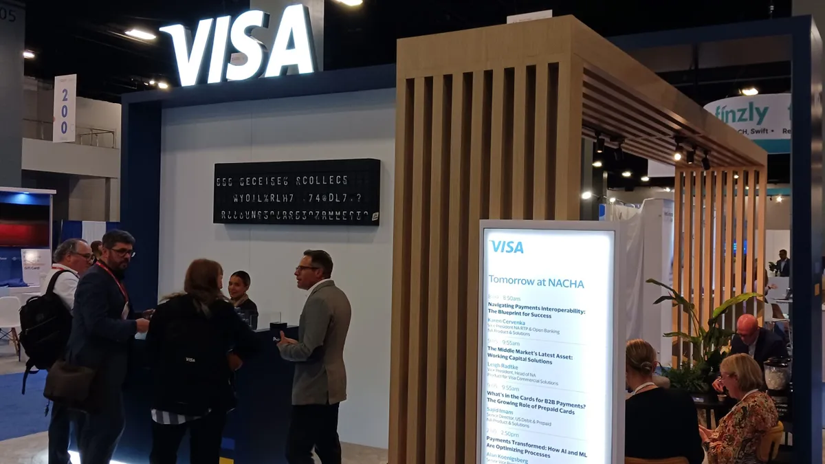 People standing at a conference booth with a Visa logo overhead.