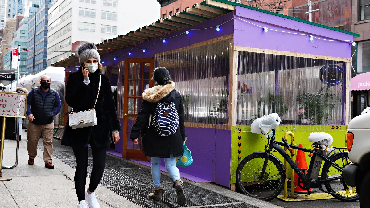 An image of a New York City sidewalk with an outdoor dining shed.