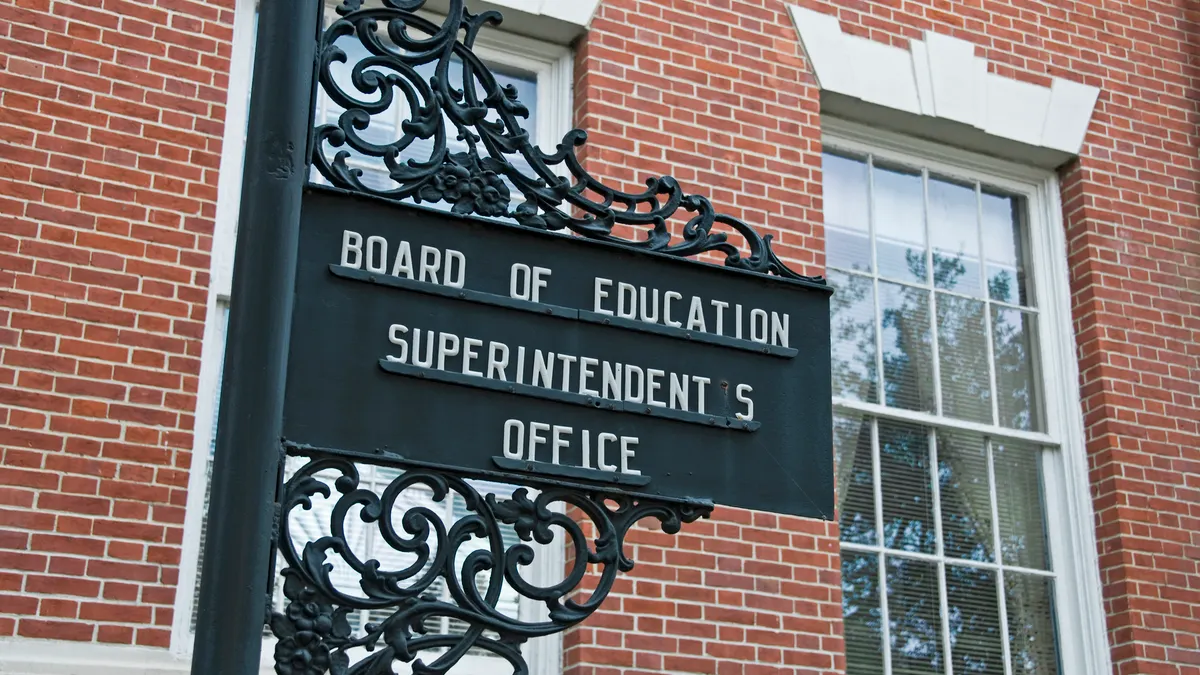 A black sign outside of a brick building denotes the structure as a board of education and superintendent's office.