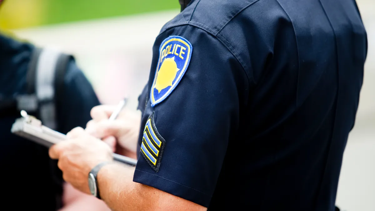 A police officer writes up a ticket to in front of a high school student.