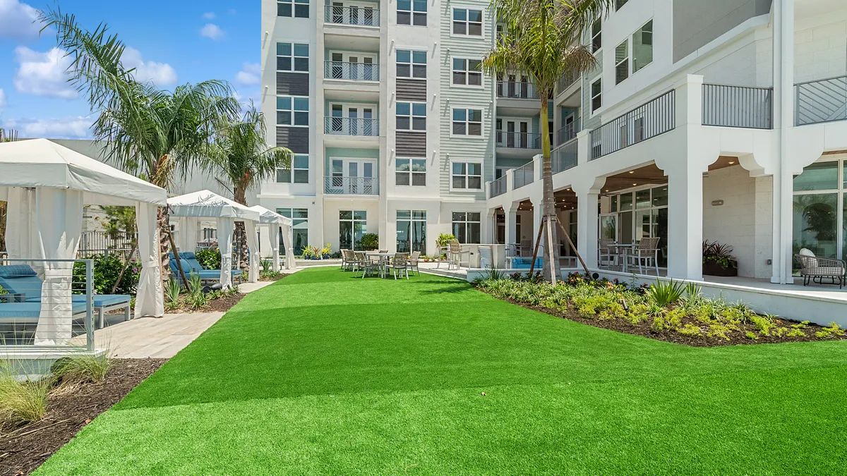 A lawn next to an apartment building, with outdoor seating along either side.