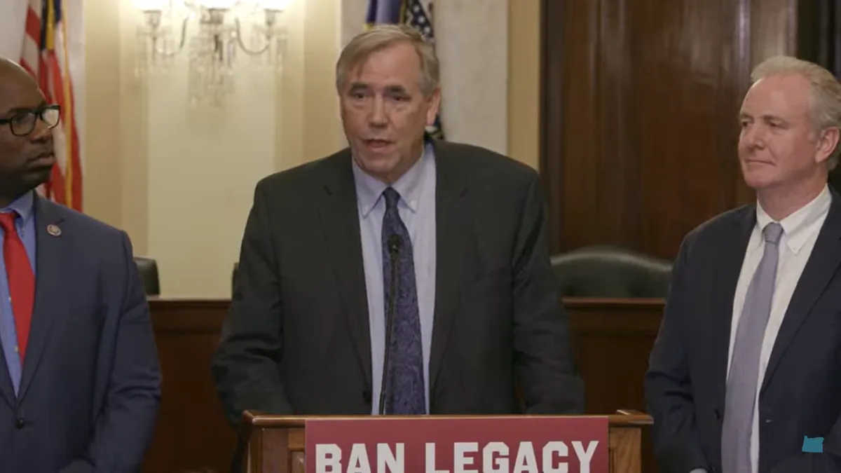 Senator Jeff Merkley speaks at podium with a sign hanging on it that calls for a ban on legacy admissions