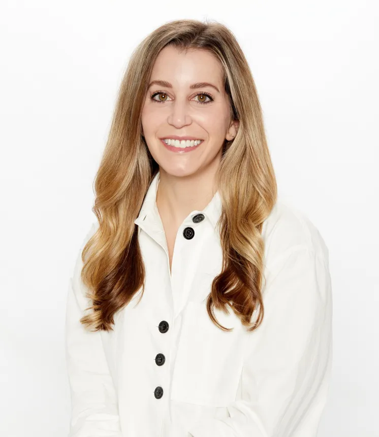 A woman, Lauren Picciano, wears a white blouse and smiles at the camera in a head shot.