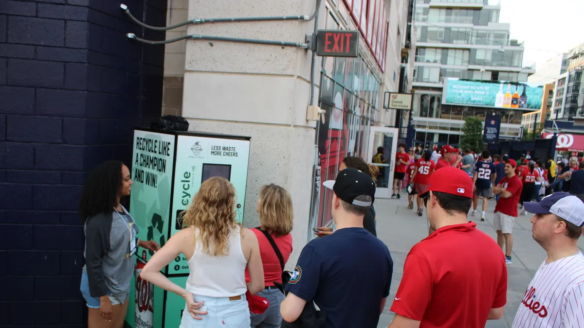 People line up to insert containers into a reverse vending machine at a sporting venue