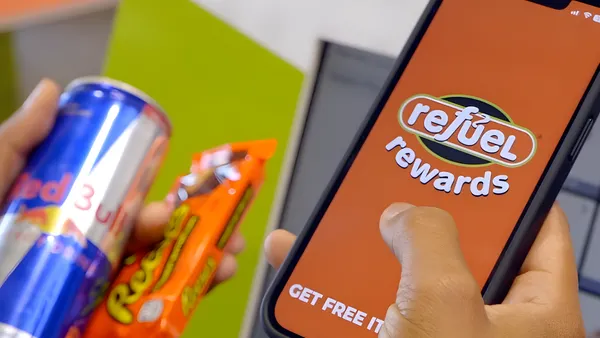 A photo of a hand holding a cell phone. Text on the phone screen says Refuel Rewards Get Free Items
