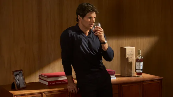 James Marsden drinks a glass of Scotch whisky as he leans against a wood sideboard.