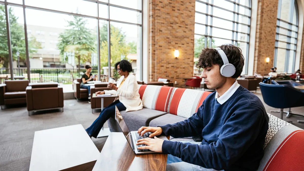 A student works on a laptop inside a campus building.