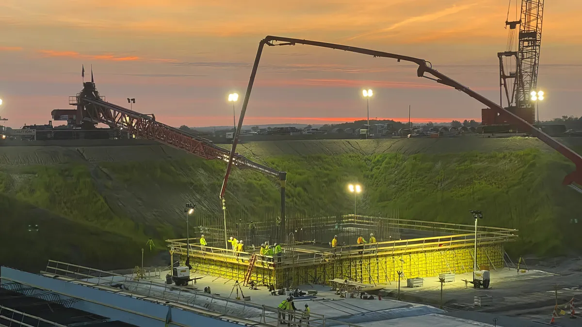 Construction workers pour concrete into the ground as the sun rises.