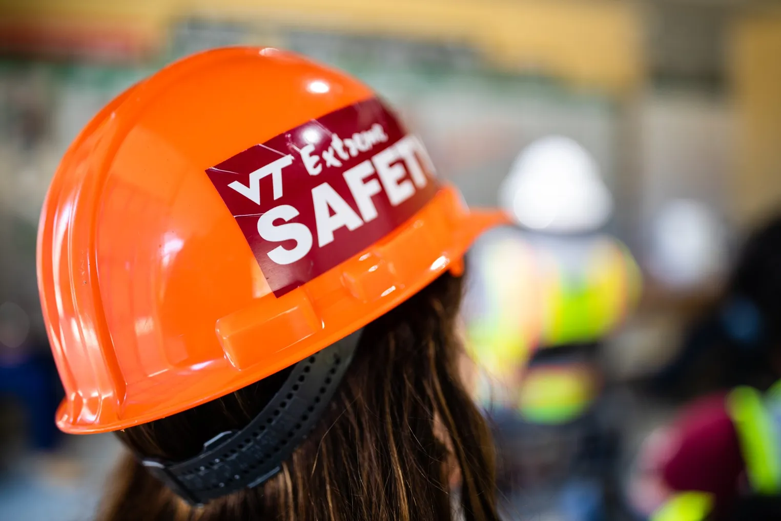 The back of a person's head wearing a bright orange Virginia Tech construction helmet.