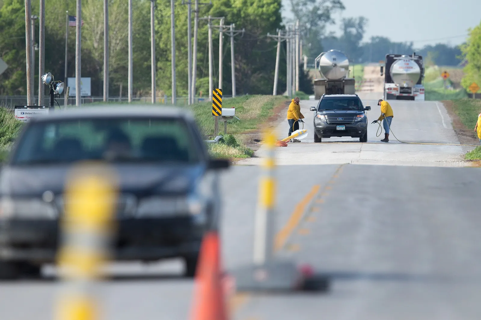 A car is sprayed down by two people on a road in the countryside.