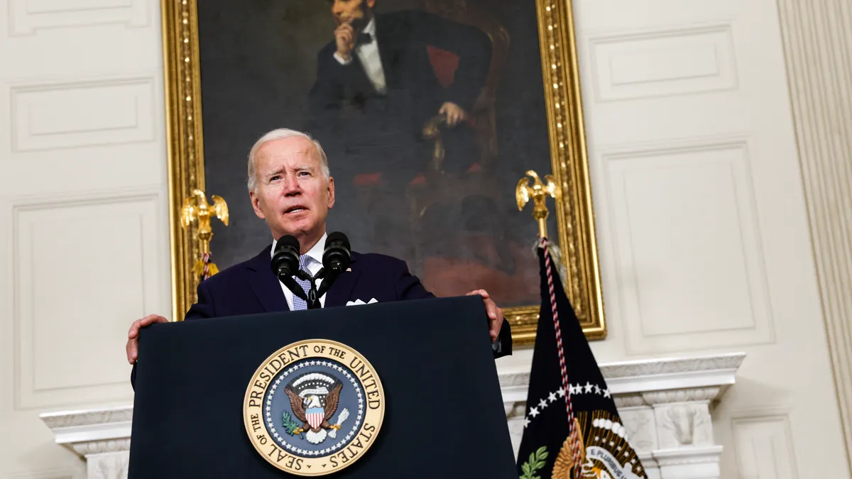 President Joe Biden stands at a podium under a painting of Abraham Lincoln