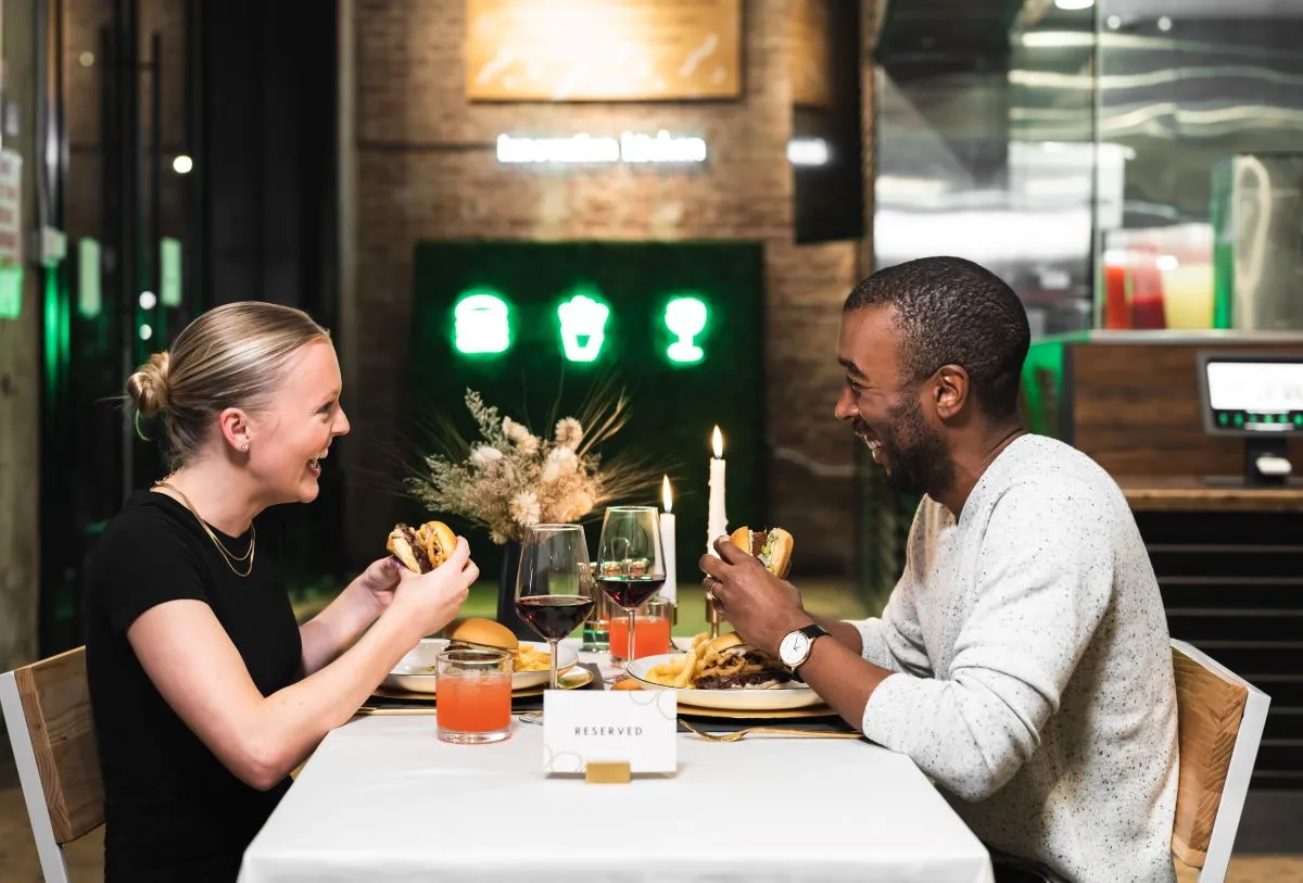 A photograph of two people at a Shake Shack eating white truffle burgers.