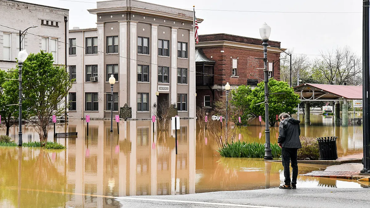 A persong in a coat overlooks a flooded city block of businesses.