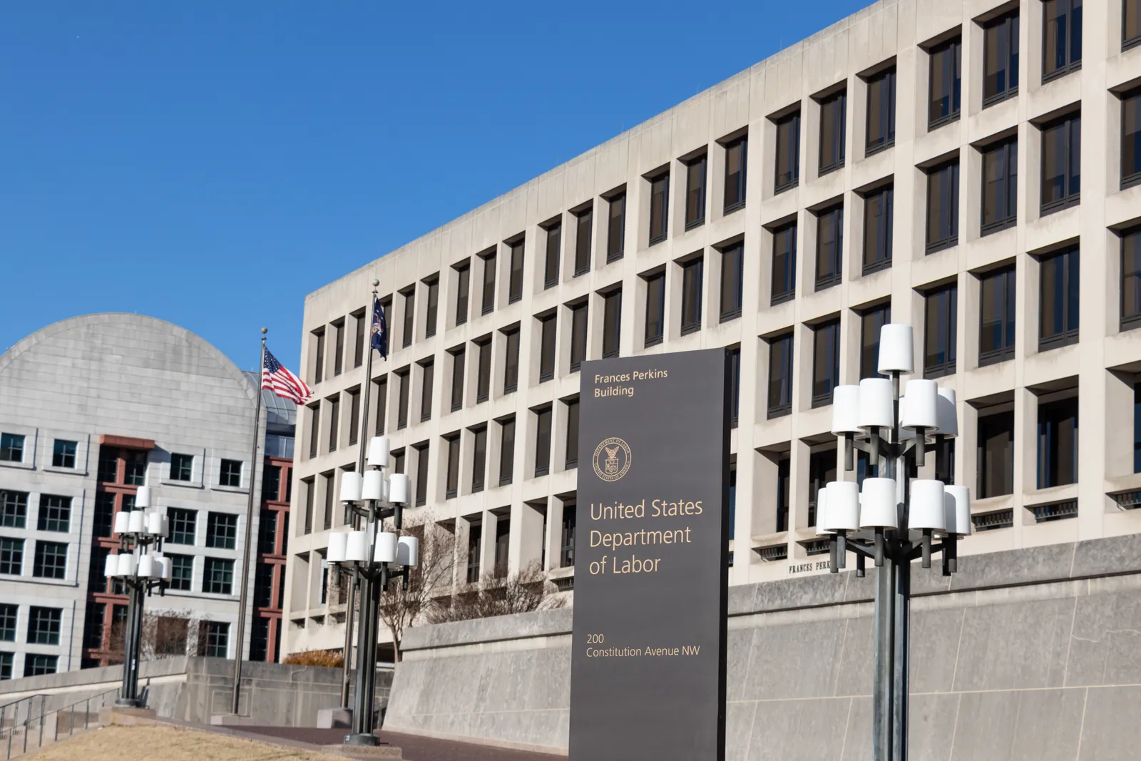 A brown Department of Labor sign in front of a beige building under a clear blue sky.