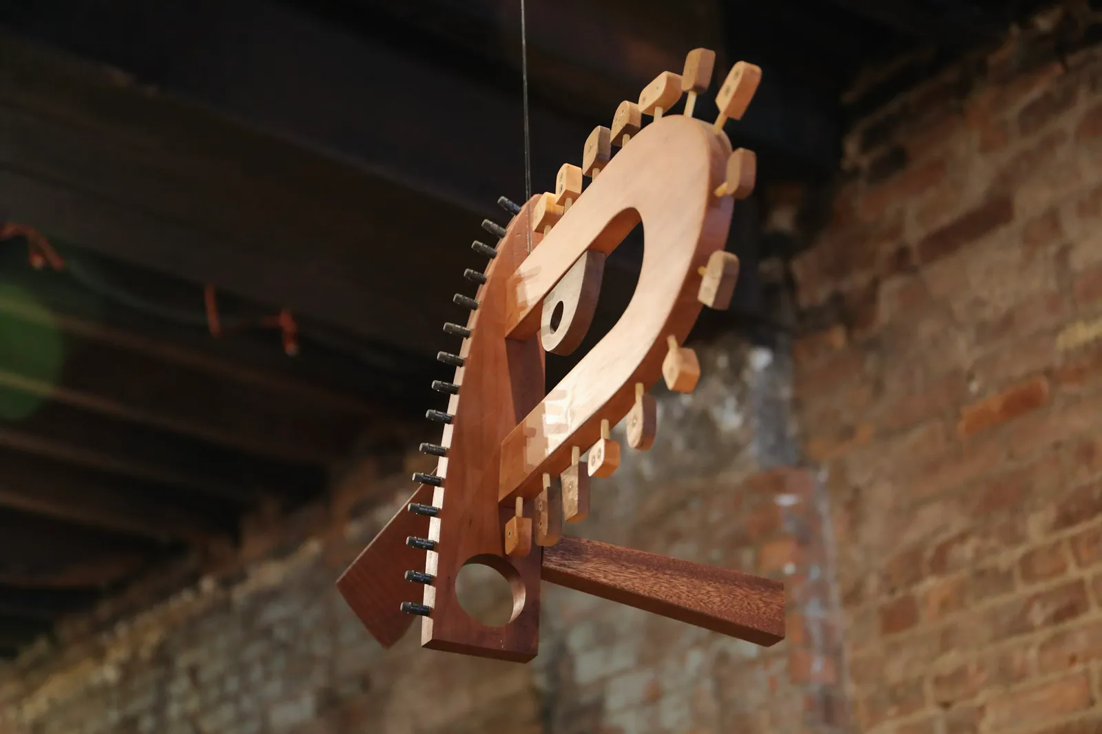 A hanging wooden sculpture composed of loops and rounded, interconnected pieces with small bits stubbled along a couple of edges.