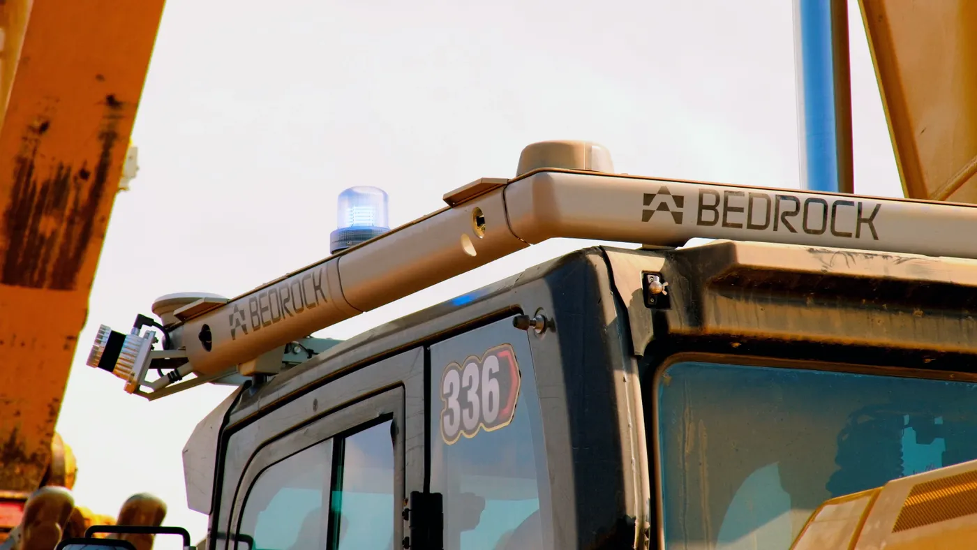 A square bar with the word "bedrock" sits atop a yellow piece of heavy machinery on a bright day.