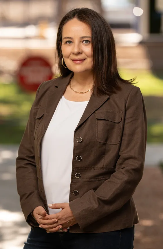 A headshot of a person in a brown jacket with a blurry background.