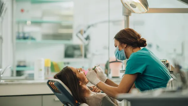 A person sits in a chair while another person examines their teeth.