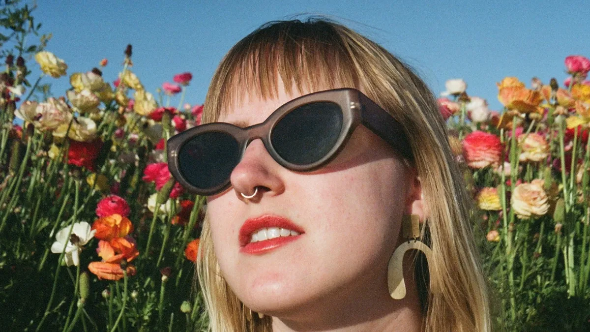 A person in a flower field with shades on looking up at the sun