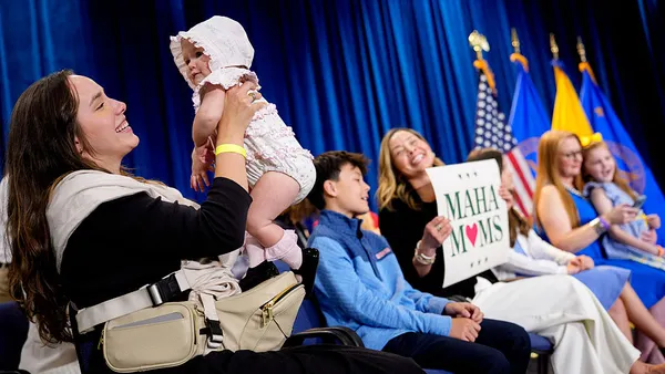 A woman holds a sign that says "MAHA Moms" next to another woman holding a baby.