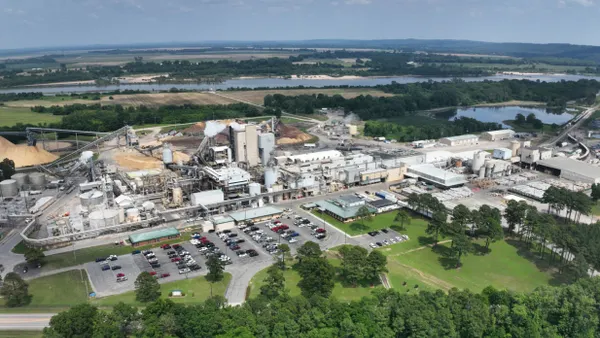 Aerial view of an industrial facility near trees and a waterway.