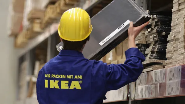 A man in a blue uniform and yellow hard hat removes a package from a shelf.