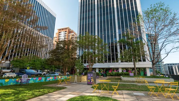 Yellow folding tables and chairs in a green space surrounded by buildings.