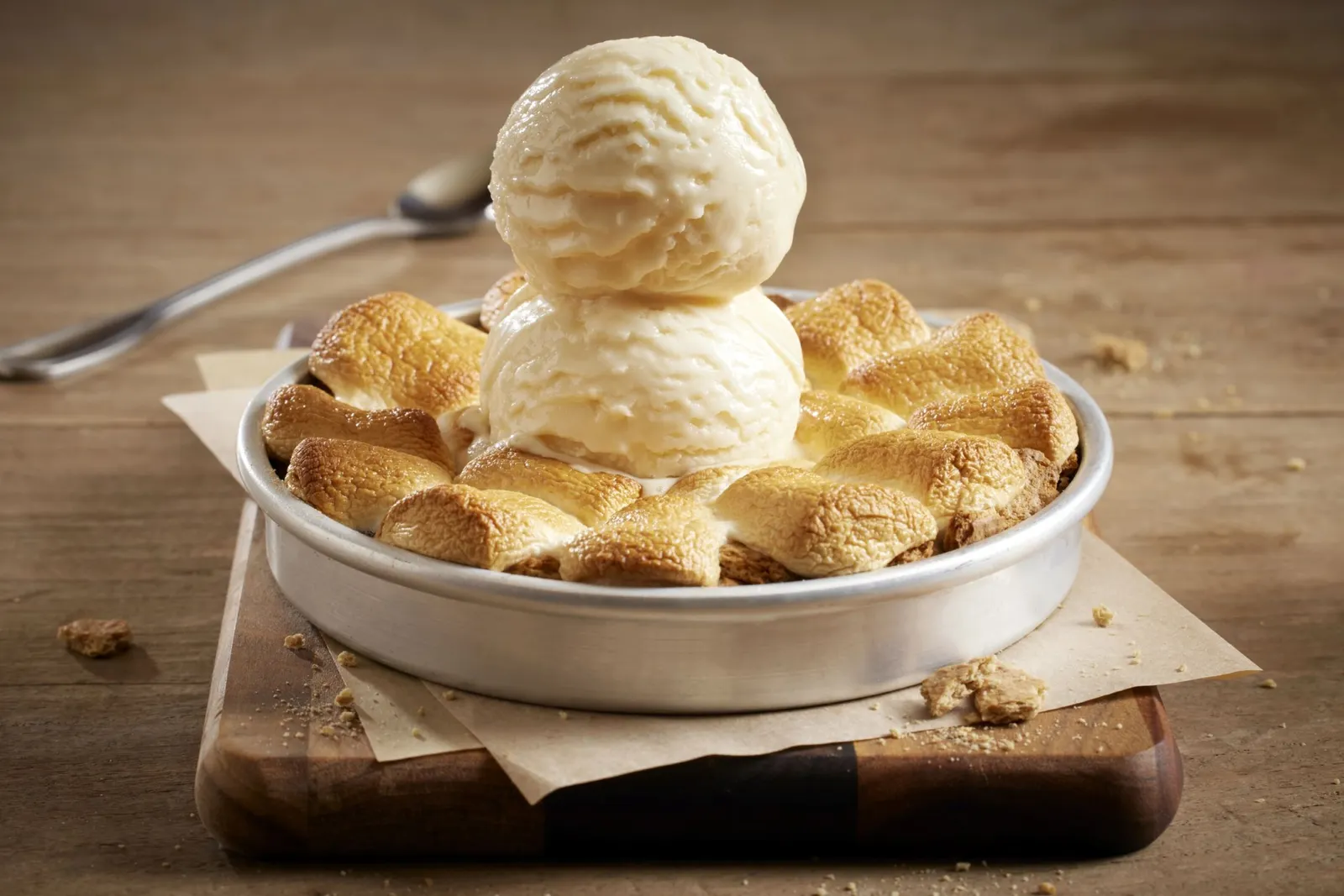 An image of a large cookie in a pan with smores on top with two scoops of ice cream.