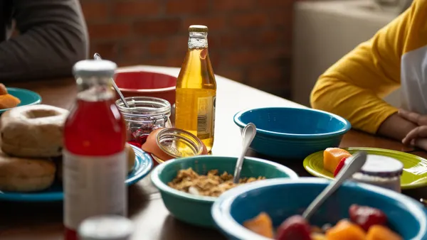 Breakfast table with bowls of fruit and granola, bagels, jam jars, and a glass bottle of juice on colorful plates and bowls