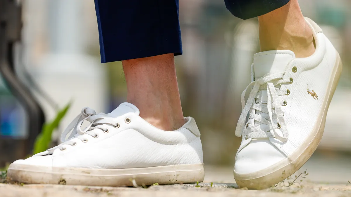 A closeup of a person wearing cropped pants and white sneakers with a polo player logo on the side of sneaker.