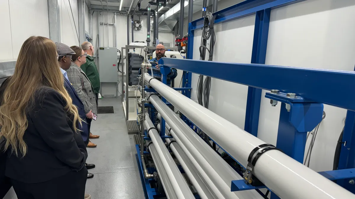 a group of people stand in a line in front of large white pipes in an indoor facility.