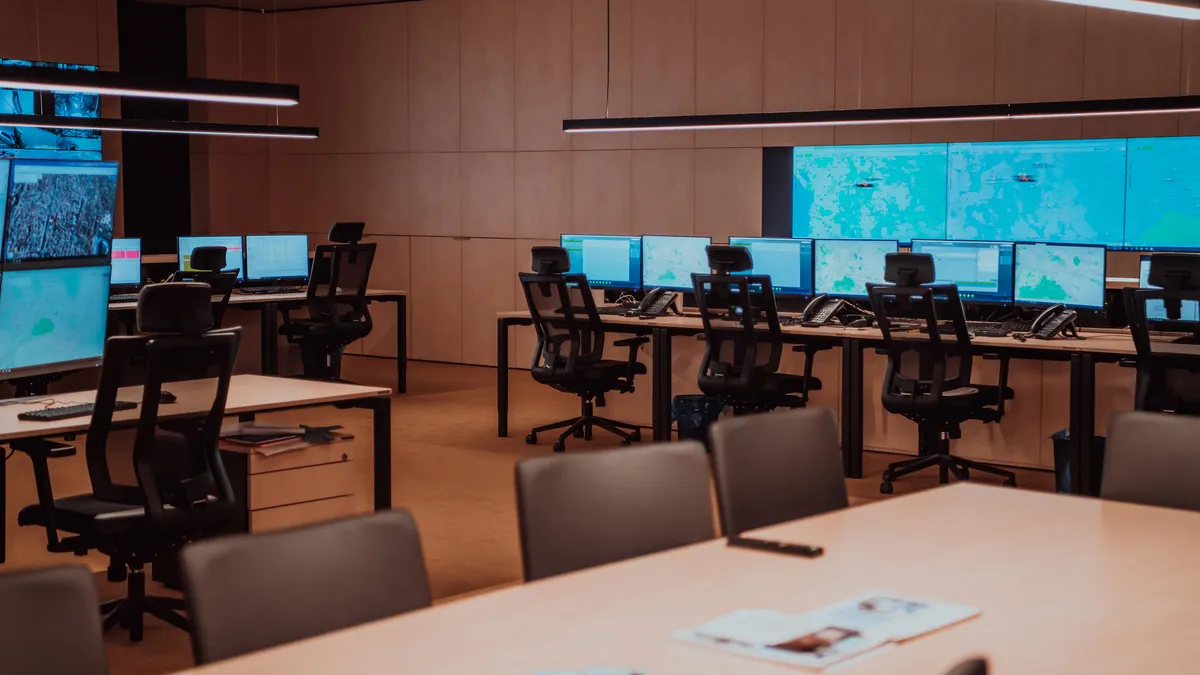 Empty interior of modern security system control room with workstations with multiple displays and big screens mounted on the wall.