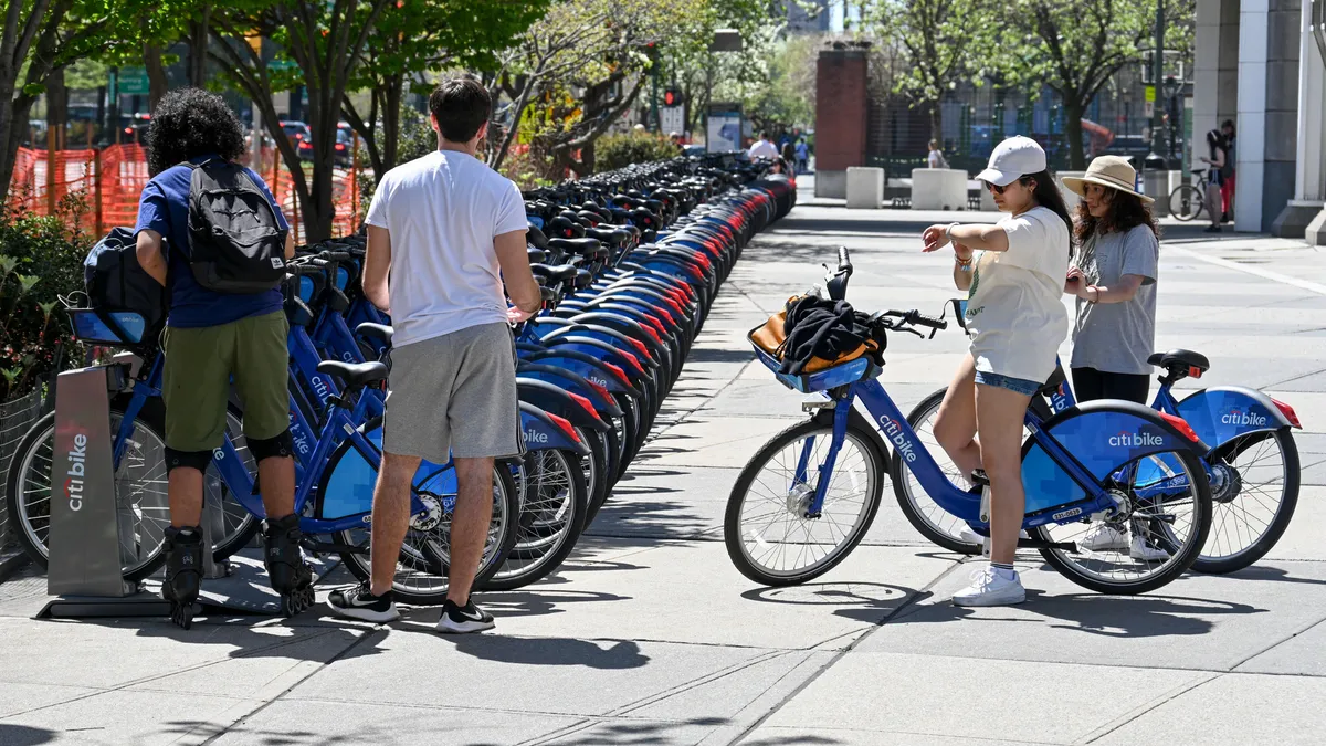 Four people stand near a rack filled with shared bikes. Two people are on bikes.