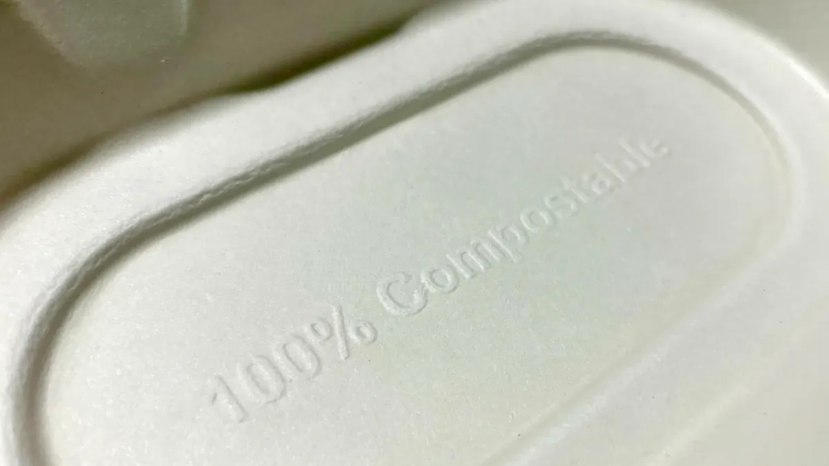 An extreme closeup of a piece of fiber packaging with "100% compostable" stamped into the material.